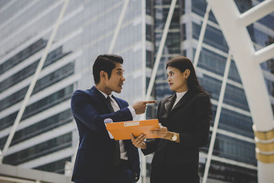 Low angle view of colleagues discussing file while standing against building in city