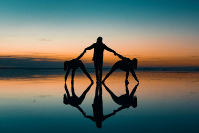 Silhouette female friends holding hands at salt flat against sky