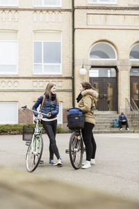 Schoolgirls with bicycles communicating outside school building