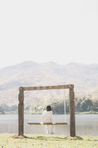 Rear view of woman sitting on swing by lake