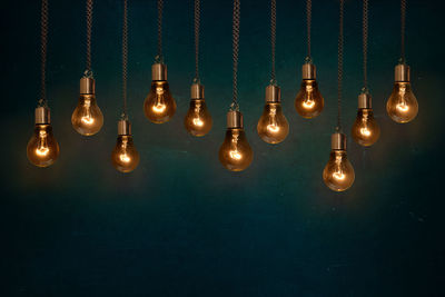 Close-up of illuminated light bulb hanging against wall