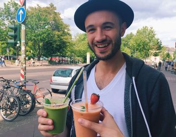 Portrait of happy young man holding smoothie at street