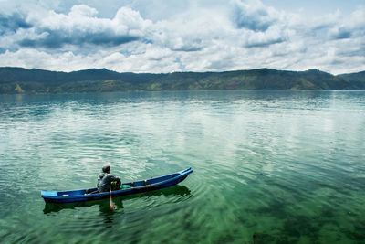 High angle view of man sitting in boat on lake against cloudy sky