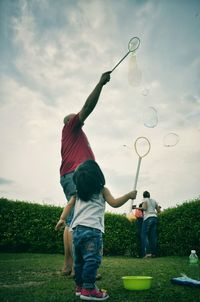 Low angle view of father and daughter making bubbles in lawn