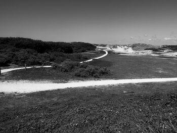 Scenic view of road amidst field against clear sky