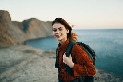 Portrait of smiling young woman standing at beach against sky