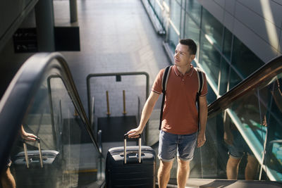 Traveler walking through airport terminal. man with suitcase standing on ecalator. 