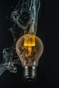 Close-up of smoke emitting broken light bulb against black background