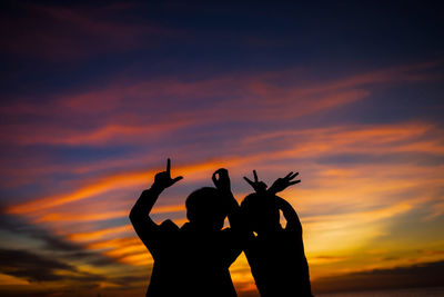 Silhouette woman with arms raised against orange sky