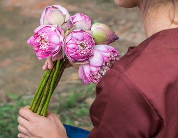 Midsection of woman holding pink lotus flowers