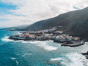 Aerial view of sea by mountains against sky