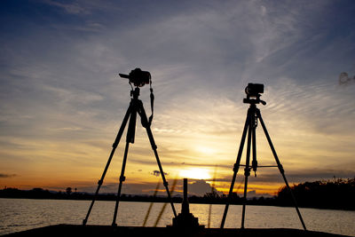 Silhouette of photographing by sea against sky during sunset