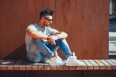 Handsome man wearing sunglasses while sitting against wall