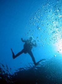 Low angle view of silhouette scuba diver swimming in blue sea