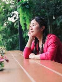 Portrait of an asian red-shirted woman relaxing casually in the outdoor garden wooden table 