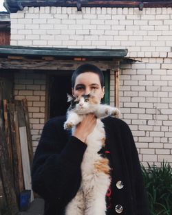 Portrait of person with a cat against a brick wall