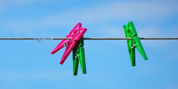 Low angle view of clothespins hanging against blue sky