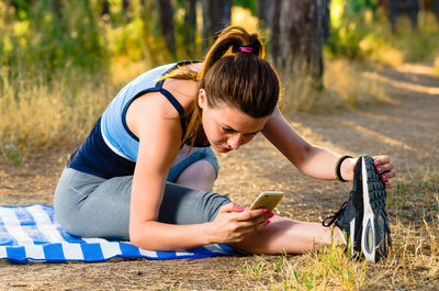 Young woman using smart phone while practicing yoga on field in forest