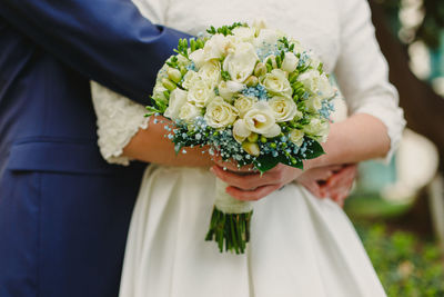 Midsection of groom embracing bride holding flower bouquet