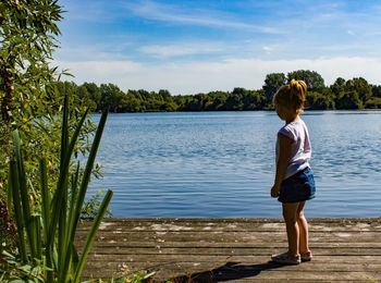 Rear view of boy standing by lake against sky