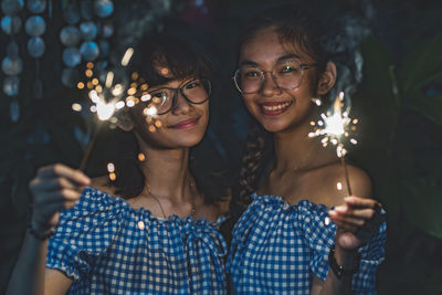 Portrait of smiling people holding sparklers at night