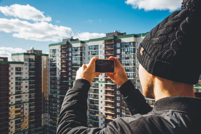 Man photographing with mobile phone against sky