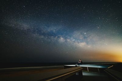 Man sitting on retaining wall against star field at night