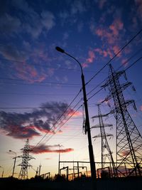 Low angle view of silhouette electricity pylon against dramatic sky