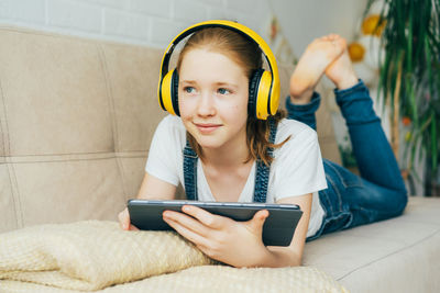 Smiling woman wearing headphones lying on bed at home