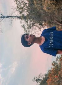 Portrait of young man looking away against trees