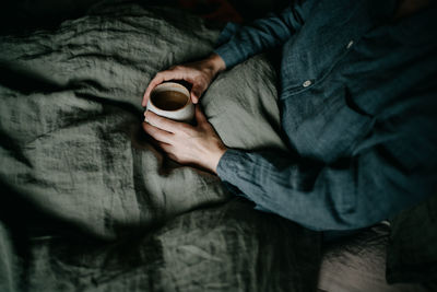 Midsection of woman holding coffee cup sitting on bed