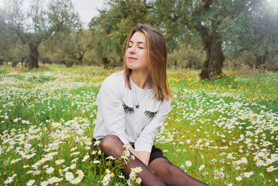 Woman sitting amidst flowers blooming on field