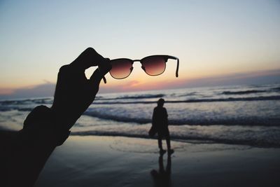 Cropped hand of person holding sunglasses at beach