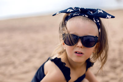 A little girl stands on the shore of the beach in a black bathing suit and black glasses
