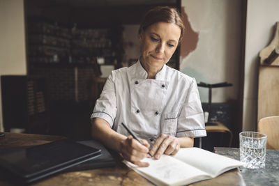 Mature chef writing in book at restaurant