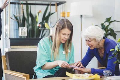 Female nurse giving manicure to senior woman at table in nursing home