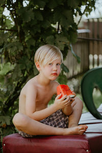 Portrait of shirtless boy holding food sitting outdoors