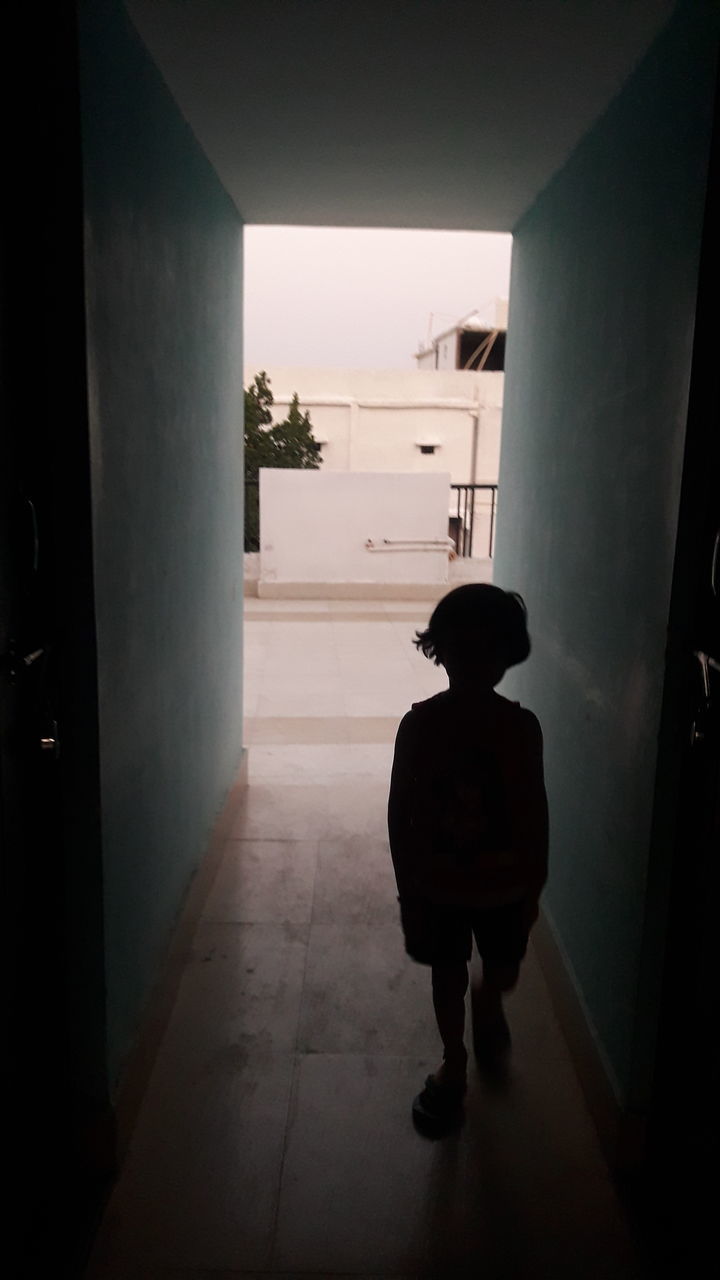 REAR VIEW OF BOY STANDING IN FRONT OF BUILDING