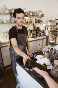 Male owner taking wireless payment from customer at checkout counter in cafe