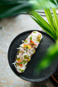 From above festive decorated colorful sandwiches with red radish sliced and herbs in white sauce served on black plate