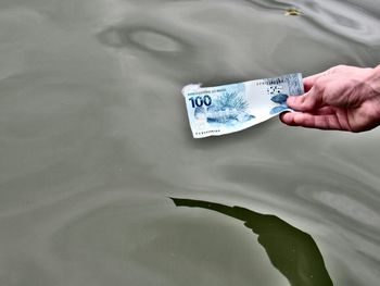 Cropped hand holding paper currency by lake