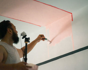 Man holding camera while painting on wall