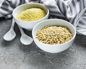 Raw couscous in a white bowl on the grey concrete background