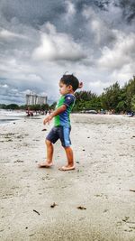 Full length of boy playing on sand at beach against sky