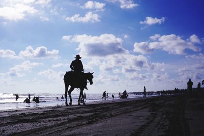 People riding on beach against sky