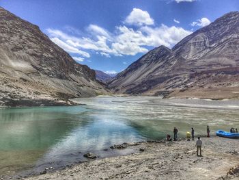 People at lakeshore by mountains against sky