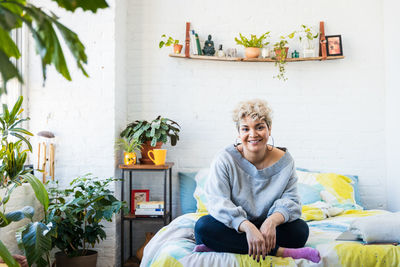 Portrait of smiling woman sitting with cross-legged on bed at home