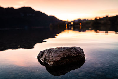 Rock in lake against sky during sunset