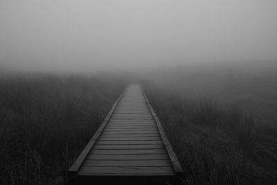 Boardwalk on landscape in foggy weather