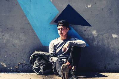 Portrait of young man sitting against wall